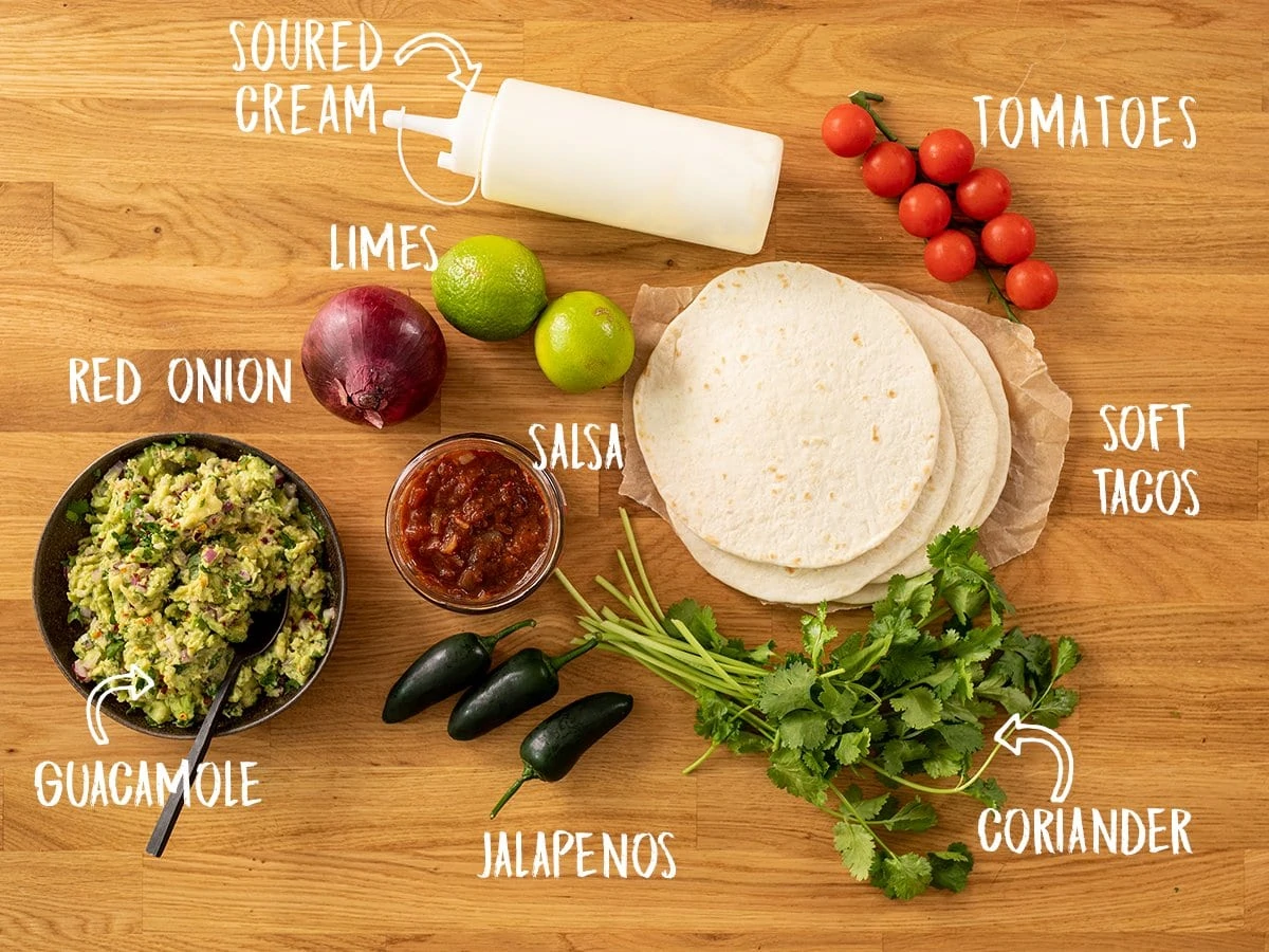 Tacos and toppings for lamb carnitas tacos on a wooden board